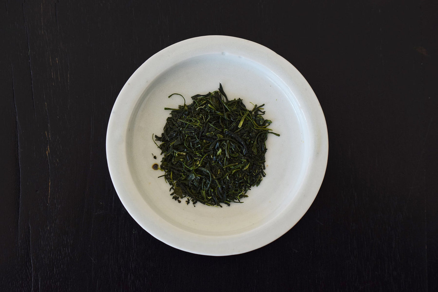 Top-down photo of a white bowl containing loose leaf green tea (No.2-41 蒸製玉緑茶 あさつゆ) on a dark surface.