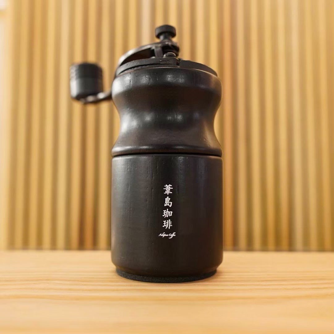 Black hand coffee grinder with a Japanese logo on the body sitting on a wooden surface.
