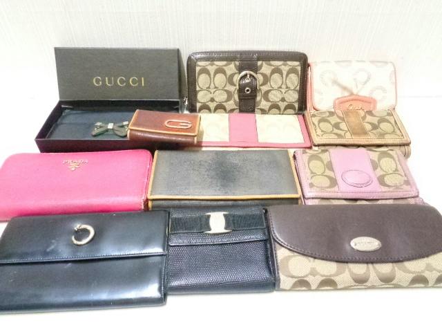 A laid-out assortment of branded wallets and key cases on a surface with a GUCCI box in the background.