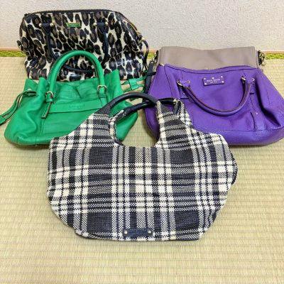 Assorted branded bags including kate spade, showing a black-and-white plaid bag, a green bag, and a purple tote arranged on a mat.