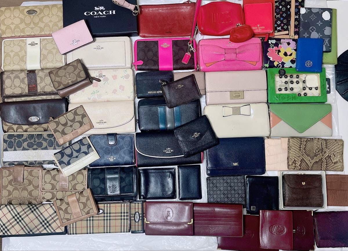 Overhead photo showing many assorted branded wallets and small leather goods arranged together as a bulk set.