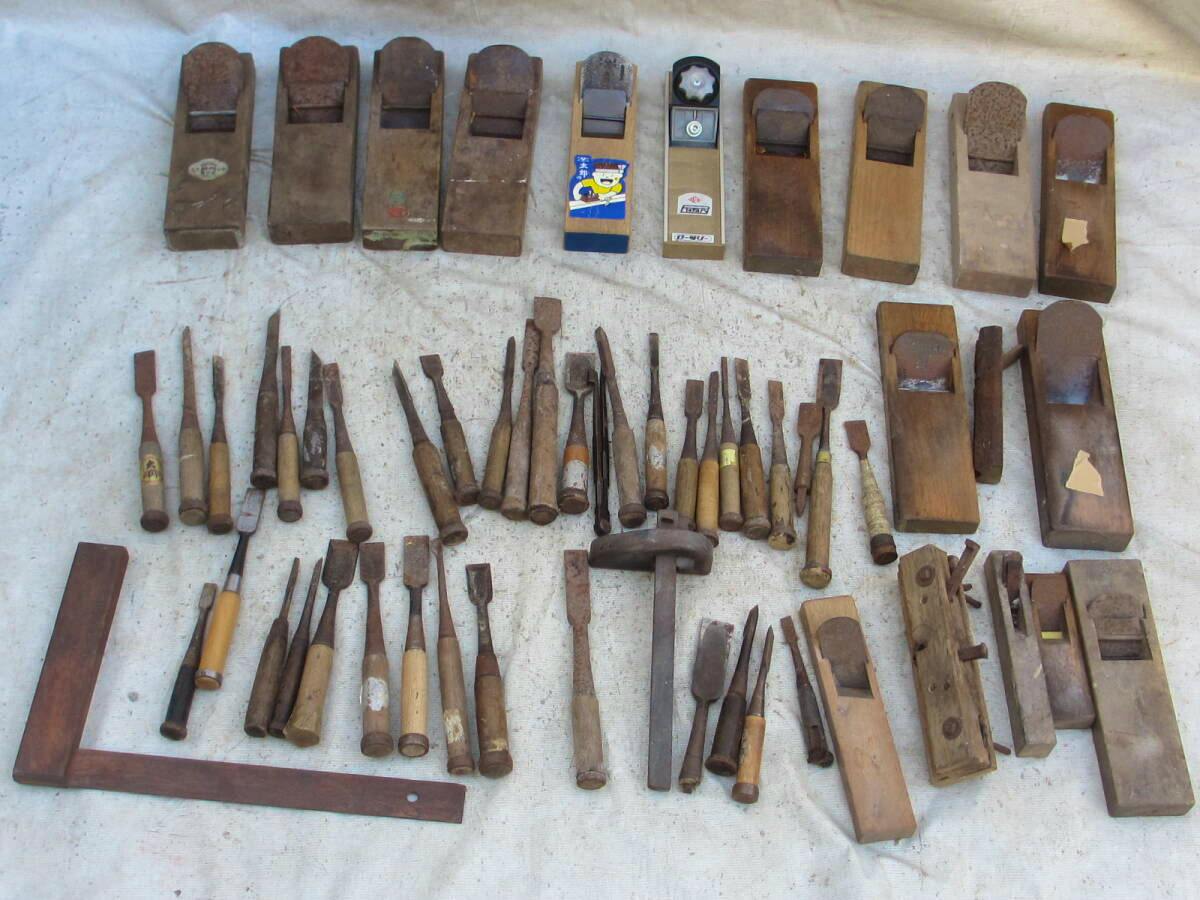 A collection of wooden hand planes and chisels arranged on a white cloth, showing a set of used carpenter tools.