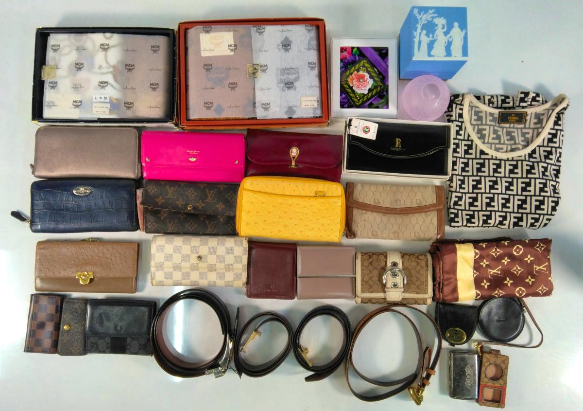 A flat lay of many branded small items—wallets, belts, scarves, and boxes—showing Louis Vuitton monogram canvas among the assortment.