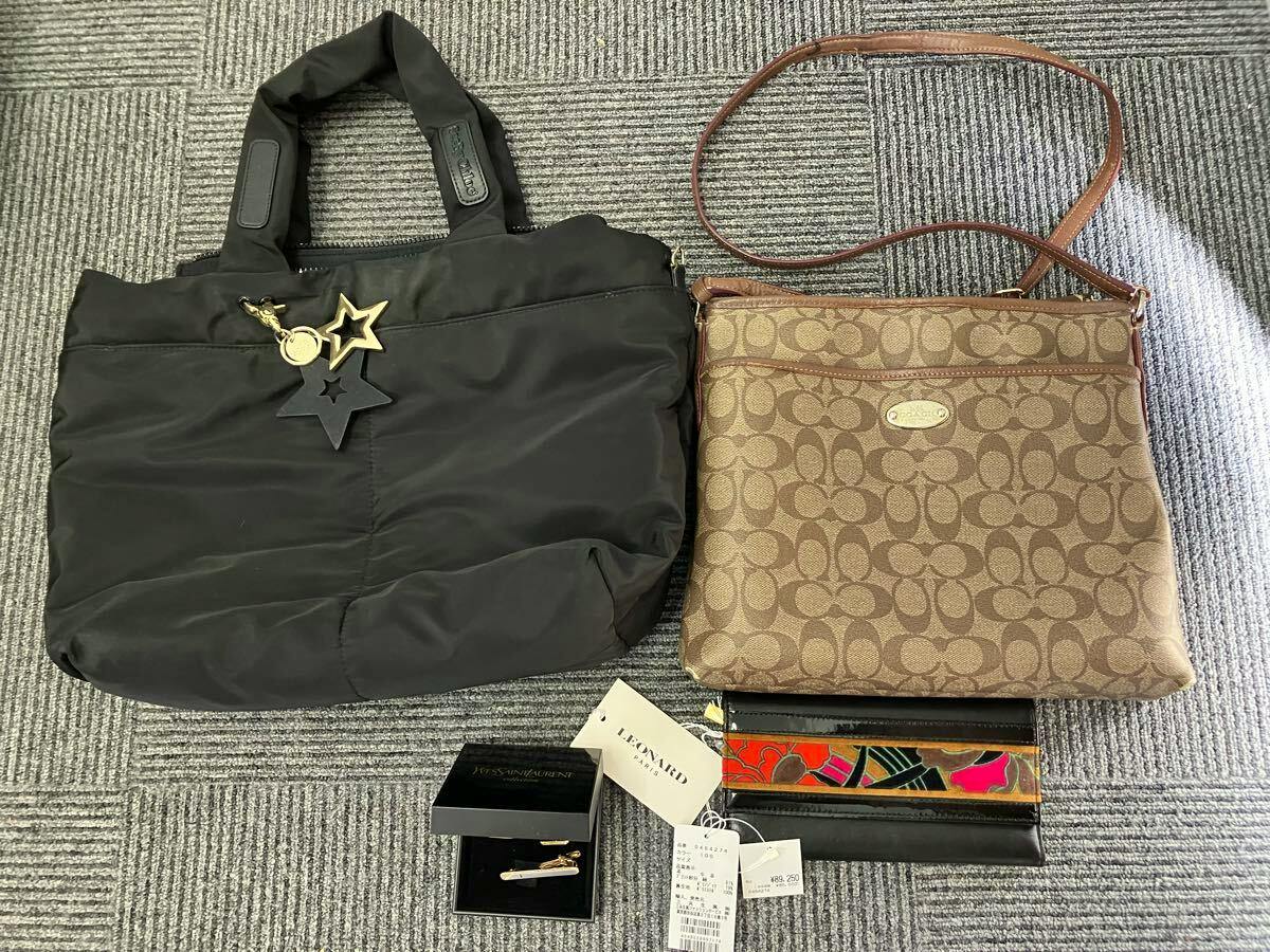 Two bags on a carpeted floor: a black tote with star charms (left) and a brown Coach monogram crossbody (right) with a wallet and tags below.