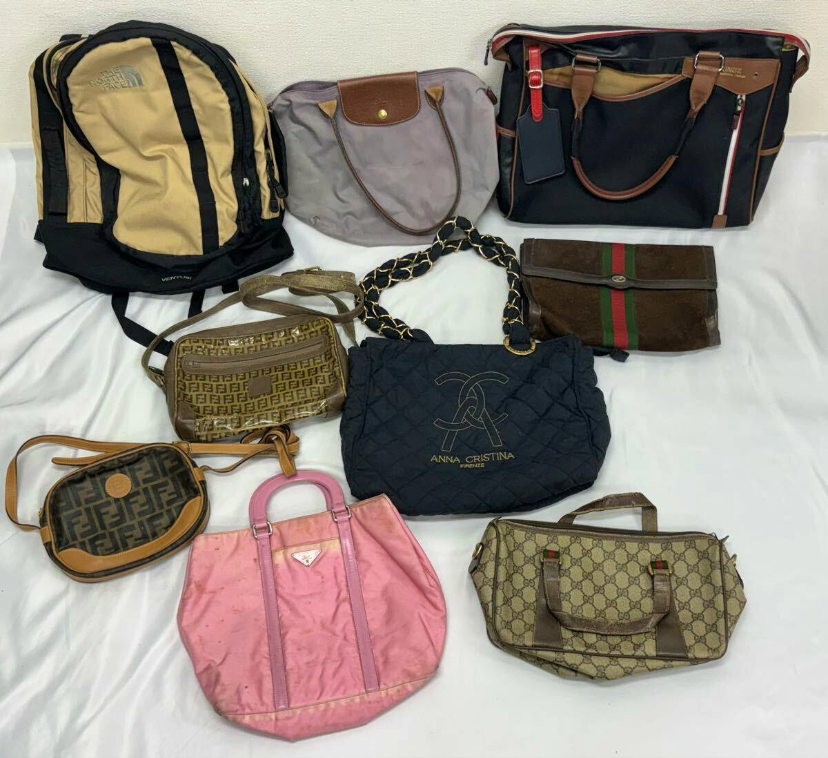 Multiple assorted branded handbags, shoulder bags, and backpacks laid out on a white surface.