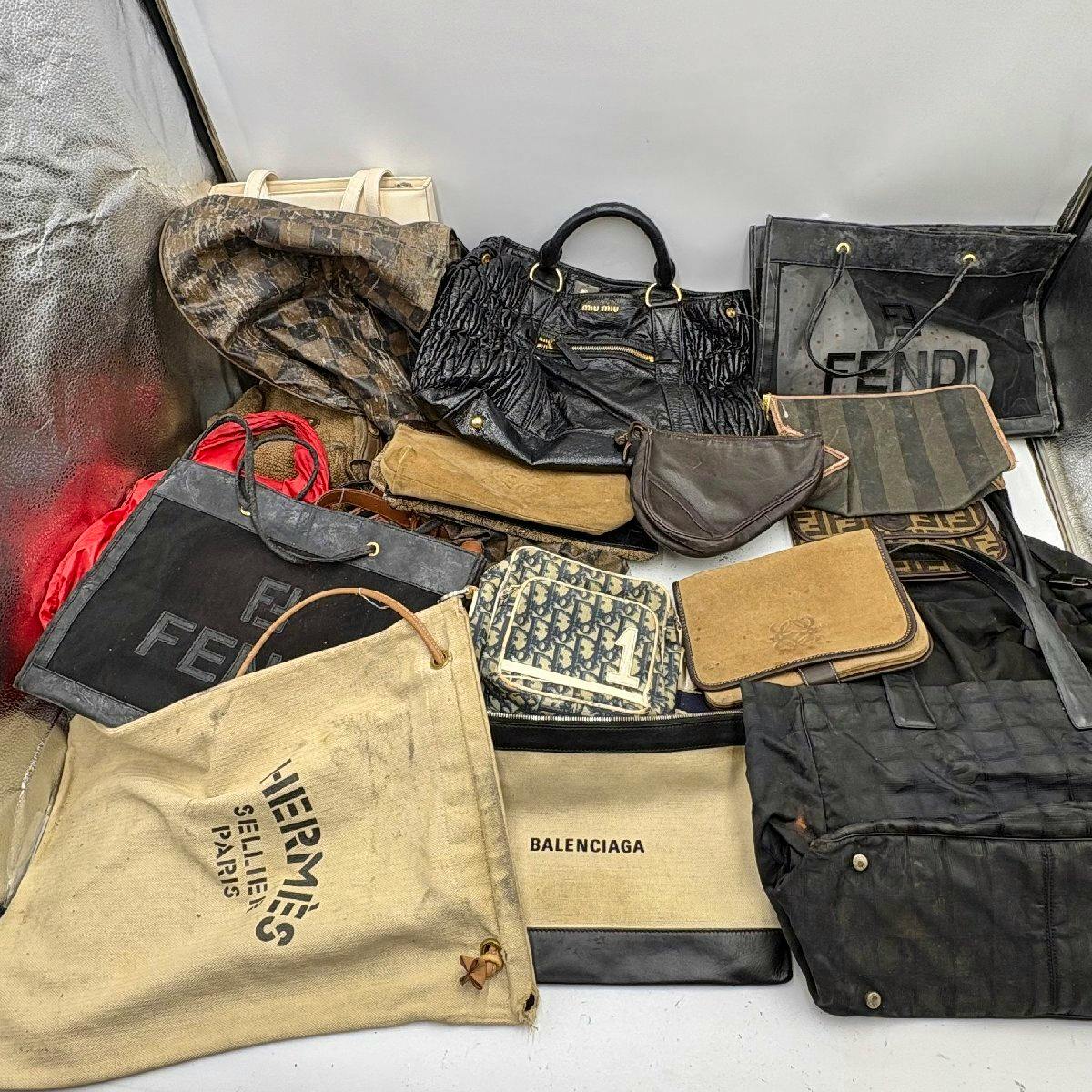 Assorted handbags and branded dust bags arranged together, with visible BALENCIAGA dust bag and FENDI and HERMÈS markings.