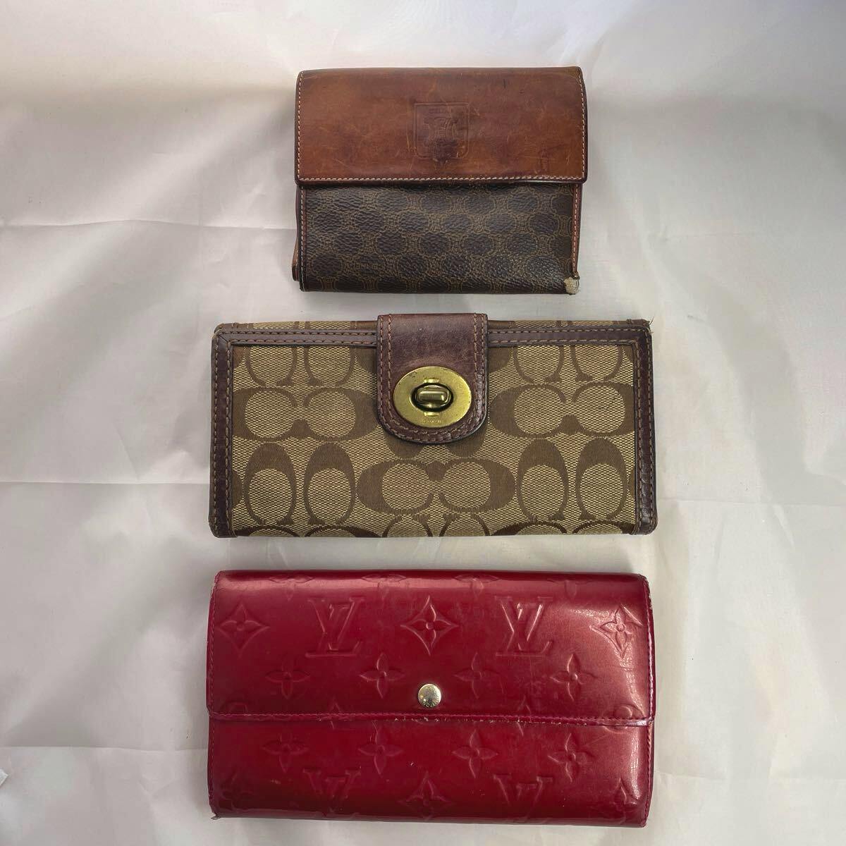 Three wallets (a brown leather wallet, a Coach canvas wallet, and a red Louis Vuitton wallet) displayed on a white background.