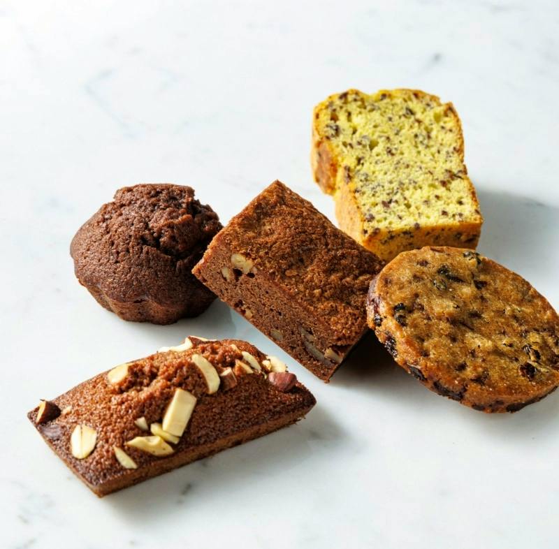 Five small travel cakes of assorted flavors arranged on a white marble surface.