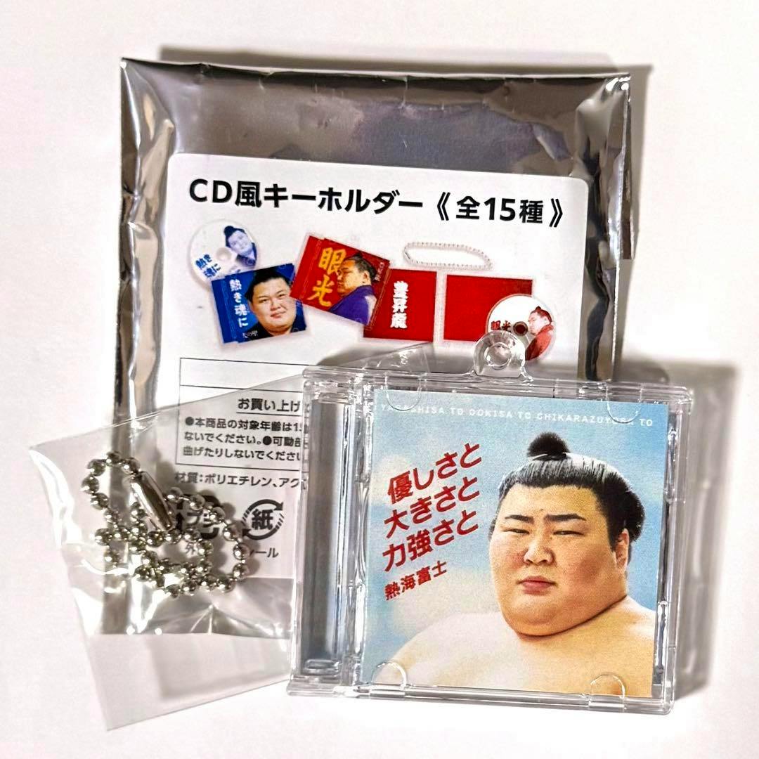 CD-style acrylic keychain showing a sumo wrestler cover, displayed with its metal ball chain and silver backing packaging.
