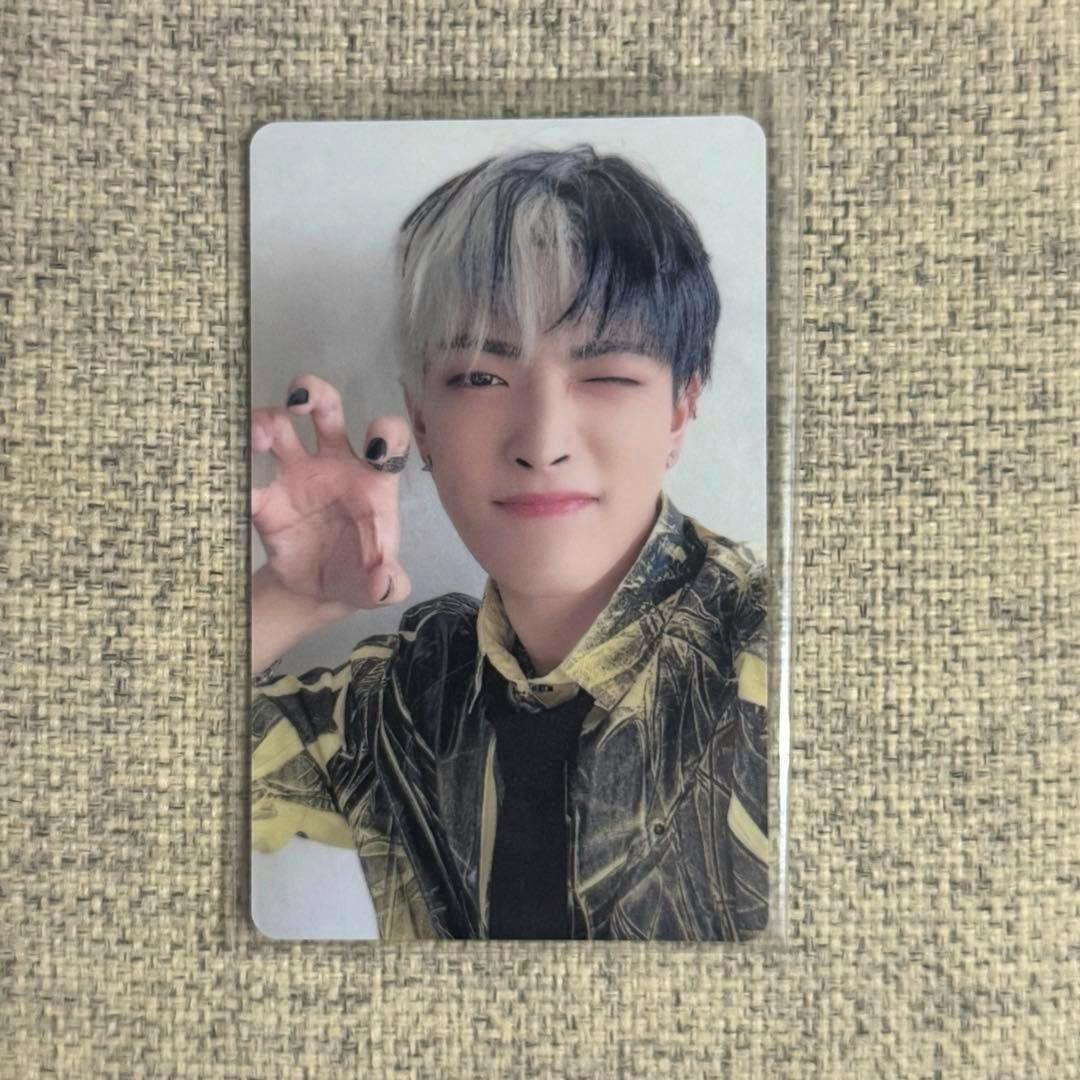 Front of a photocard showing a winking K-pop idol portrait with two-tone hair and a clawing hand pose on a textured fabric background.