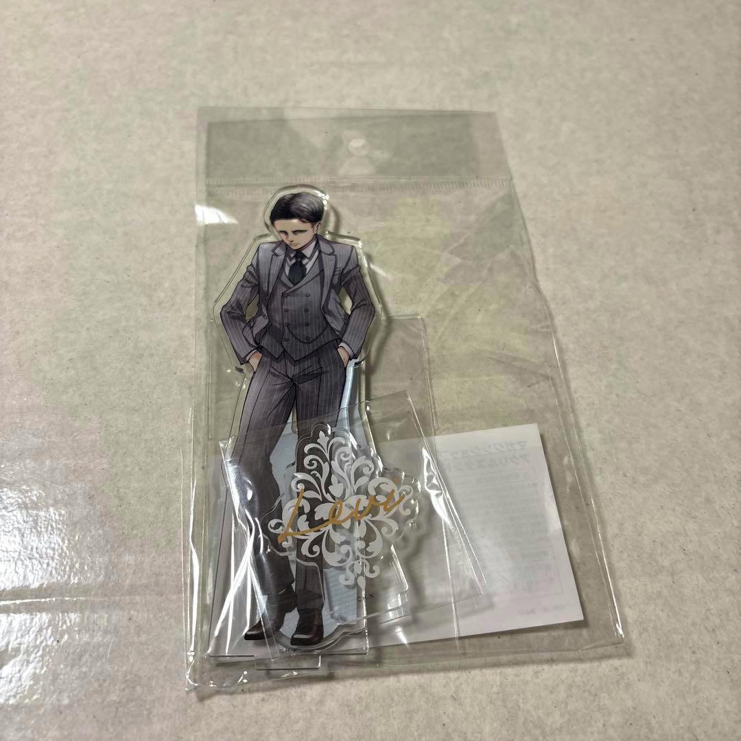 A sealed acrylic stand of Levi from Attack on Titan wearing a suit, shown in clear plastic packaging on a light surface.