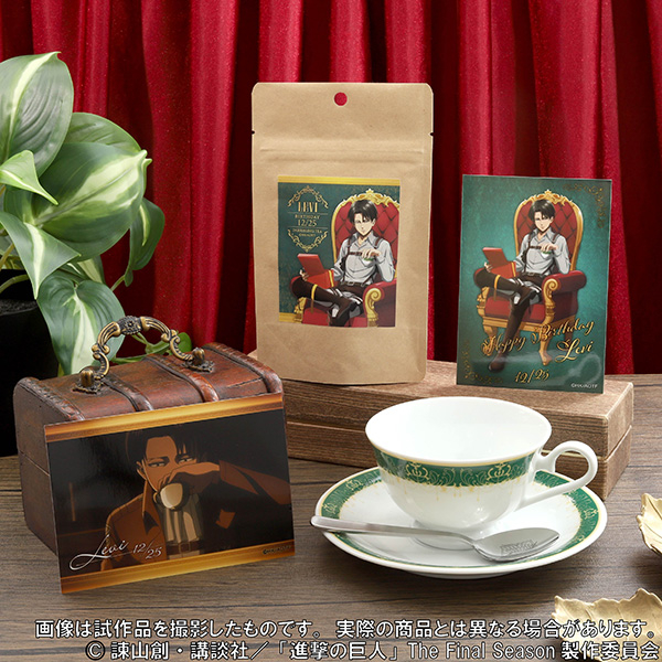 A porcelain teacup and saucer with a green decorative band displayed with a teaspoon and Levi-themed packaging and cards.