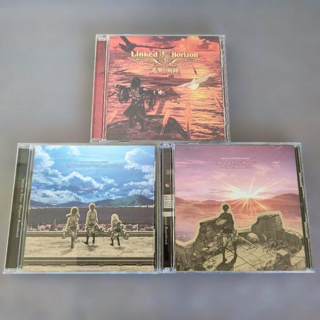 Three Attack on Titan soundtrack CD cases with cover art arranged on a gray surface.