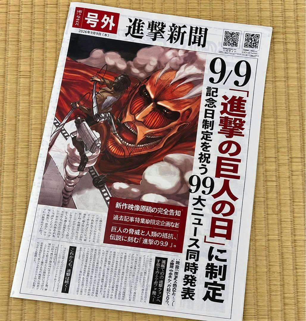 A front view of the 'Attack on Titan' commemorative newspaper-style pamphlet showing the Colossal Titan artwork and Japanese headlines, photographed on a tatami mat.