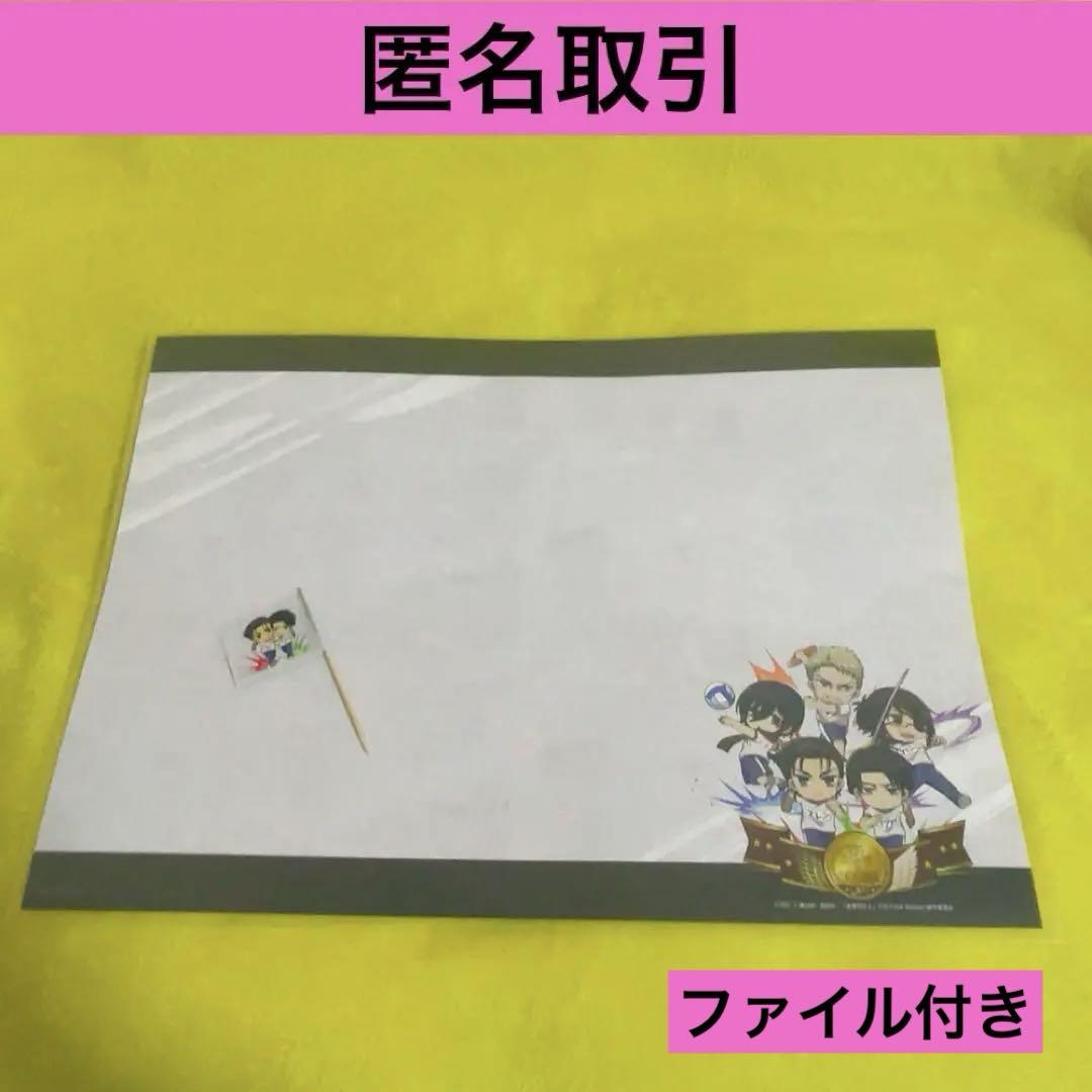 Paper luncheon mat for 進撃の巨人 (Attack on Titan) collaboration showing printed characters at the bottom right and a small flag on the left, photographed on a yellow surface.