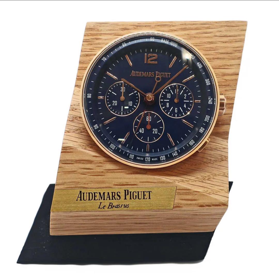 Audemars Piguet CODE11.59 chronograph table clock with a black dial set into a wooden stand bearing a brass Audemars Piguet nameplate.