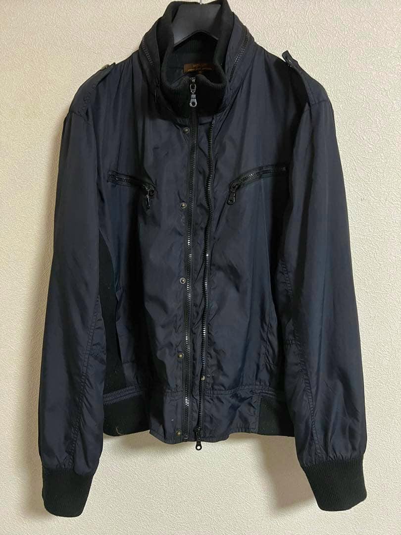 Front view of the men's nylon jacket (AUGEH IZM) in size XL hanging on a hanger against a textured wall.