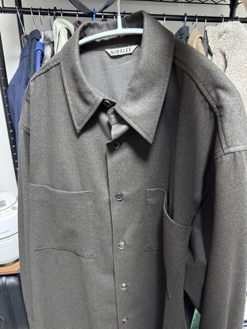 Brown AURALEE wool flannel shirt hanging on a hanger showing the front and collar.