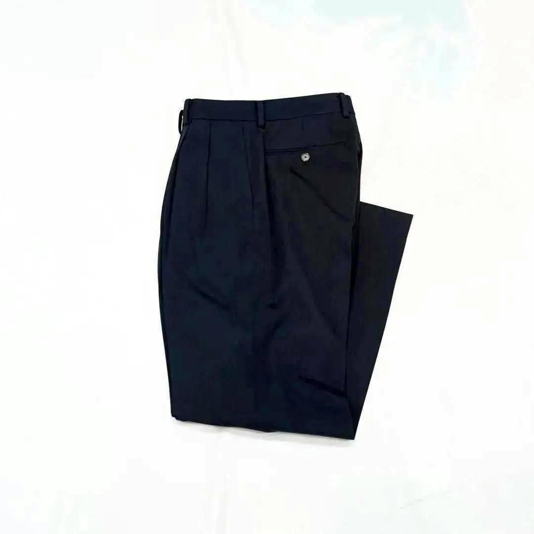 Black wool two-tuck slacks folded and laid flat on a white background.