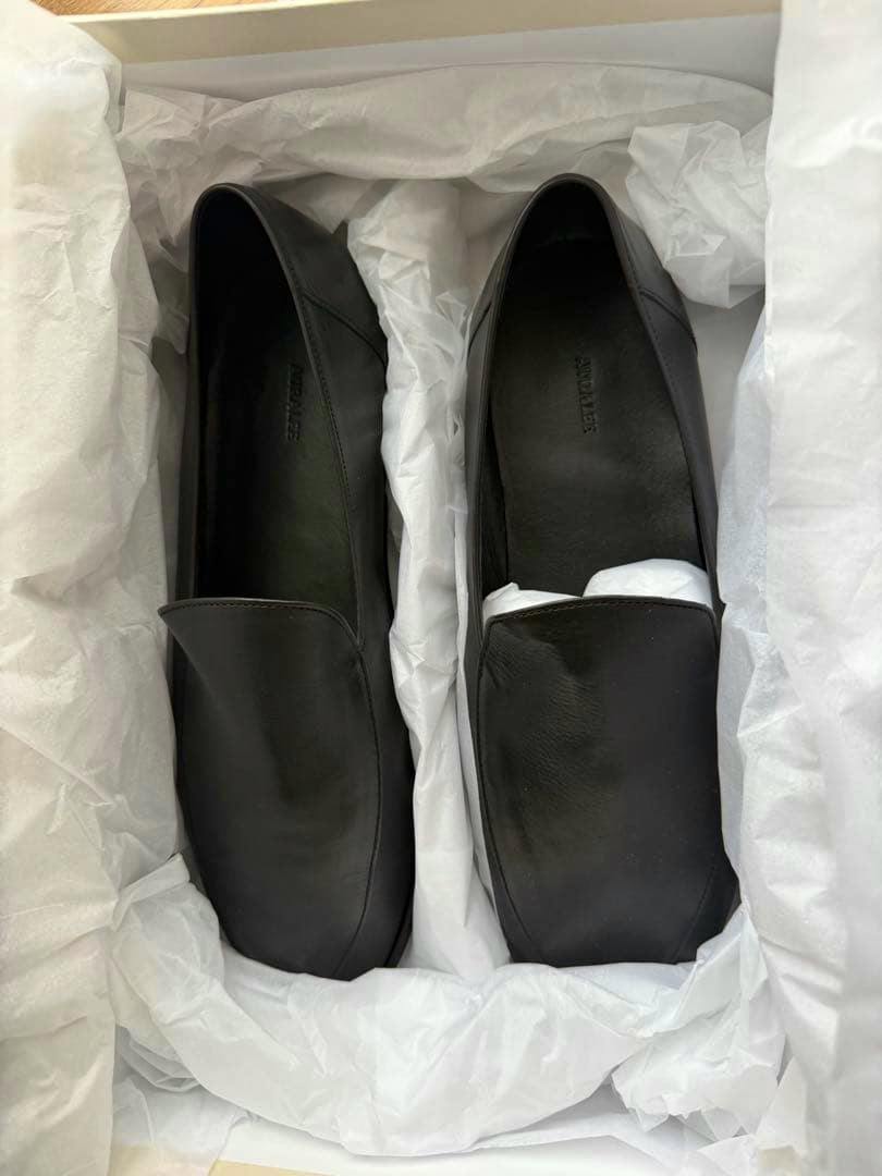 Top-down view of a pair of AURALEE soft leather loafers in a shoebox with tissue paper.