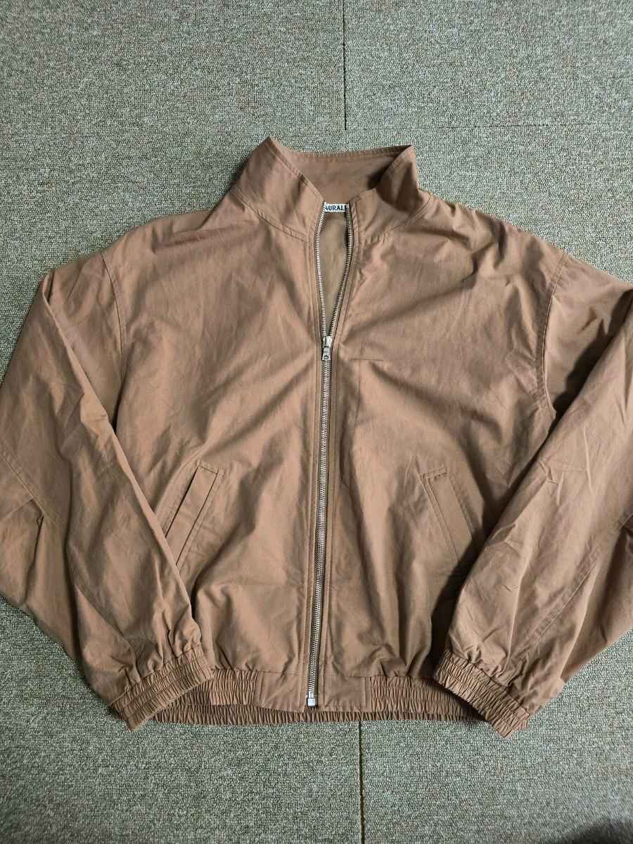 Front view of the AURALEE men's zip-up nylon jacket laid flat showing the zipper, pockets, and elastic hem.
