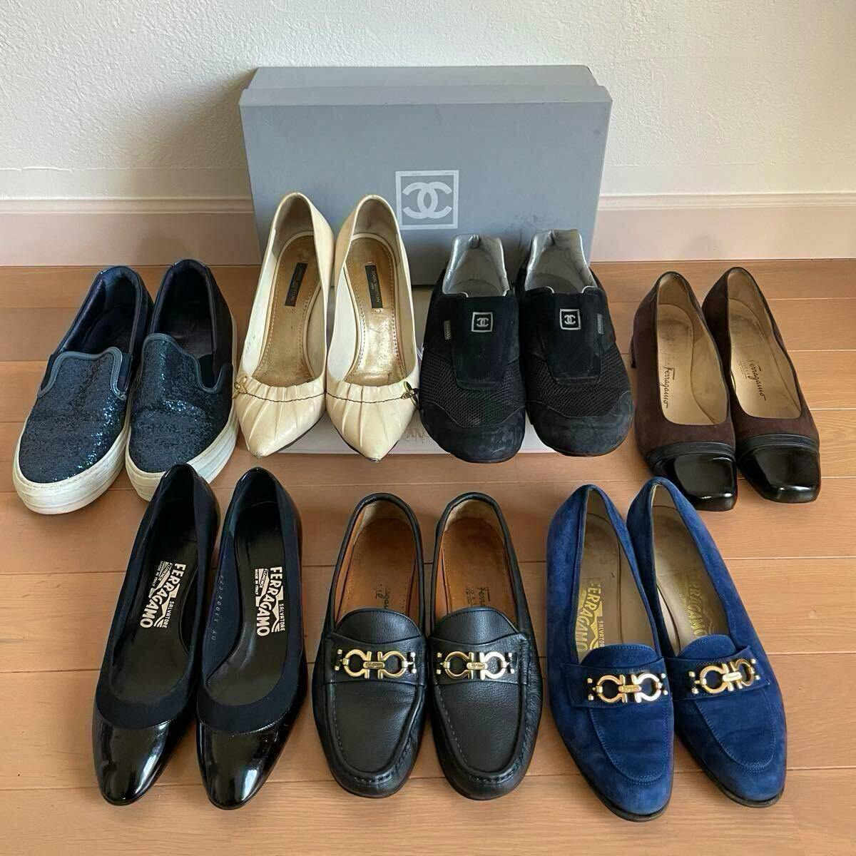 Seven pairs of shoes arranged on a wooden floor with a Chanel shoebox behind them.