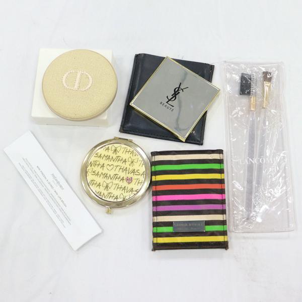 Top-down photo of a set of six cosmetic items including compact mirrors and makeup brushes on a white background.