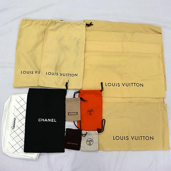 Top-down photo of a set of cotton dust bags and small drawstring pouches (including Louis Vuitton and Chanel logos) arranged on a white surface.