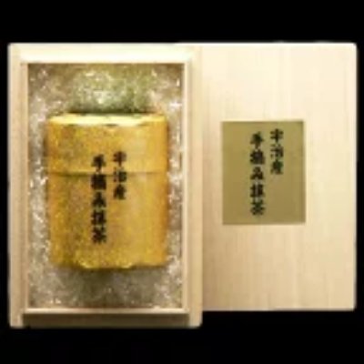 Open wooden gift box showing a gold canister of matcha tea with Japanese label and a green cloth.
