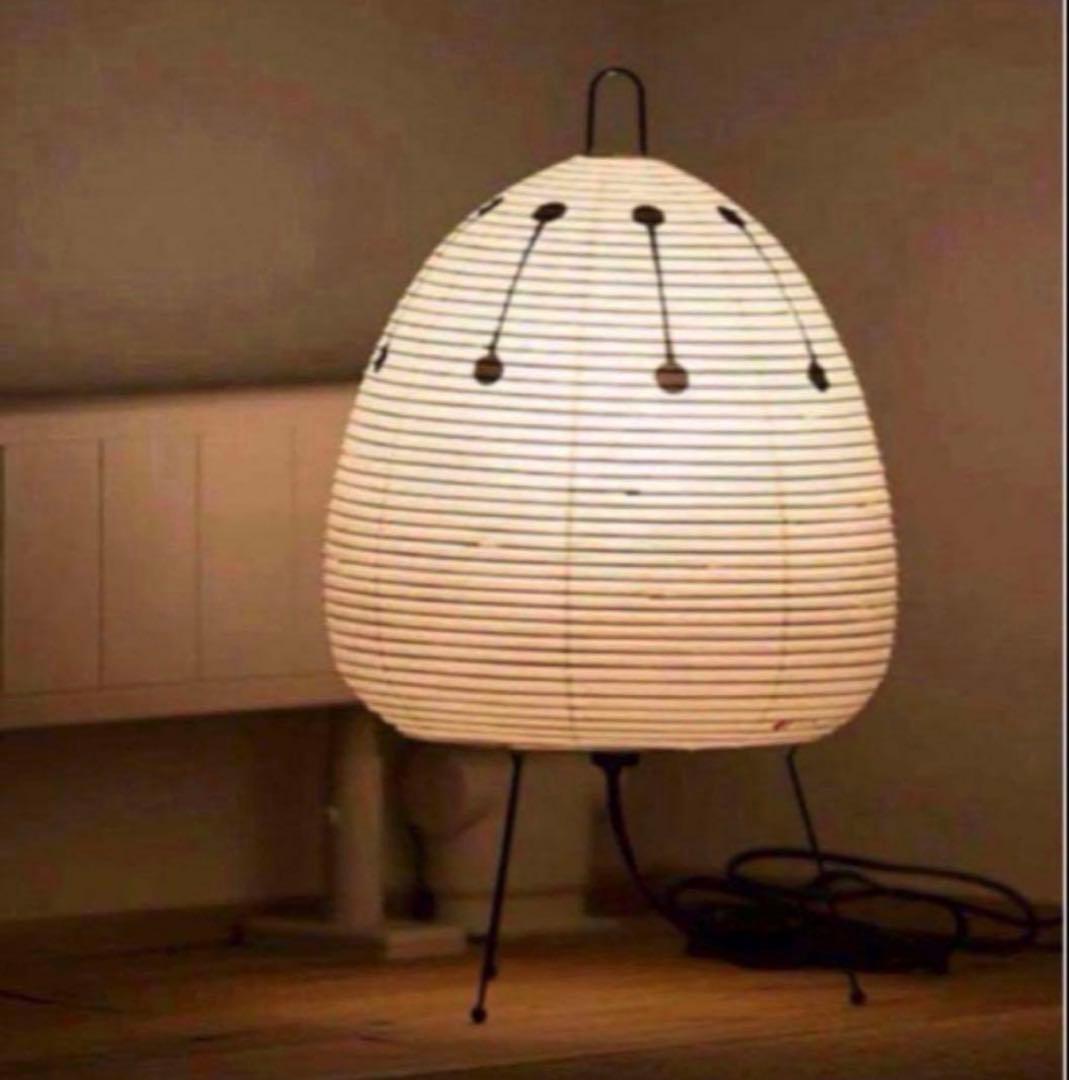 Lit Isamu Noguchi Akari 1AD floor lamp on its three-legged stand on a wooden floor.