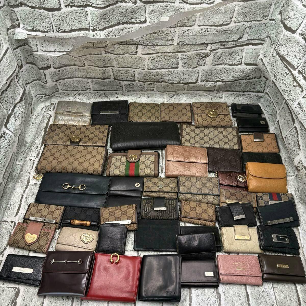 A large arranged set of Gucci wallets and small leather goods on a brick-patterned background, showing various GG canvas and leather styles.