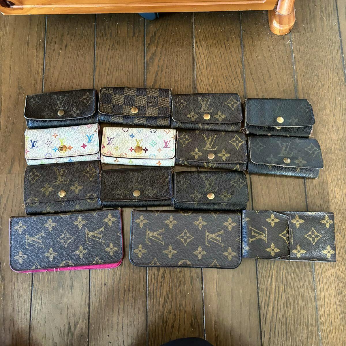 Multiple Louis Vuitton small wallets and cases in monogram and Damier patterns arranged on a wooden floor.