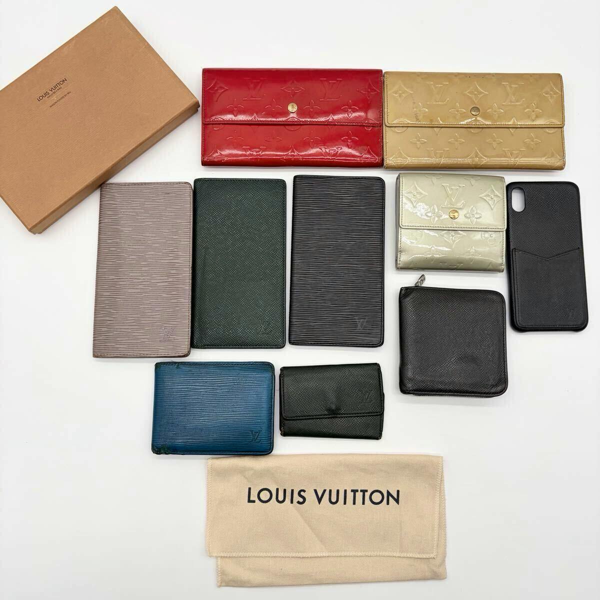 Flat lay of several Louis Vuitton wallets and small accessories arranged next to a Louis Vuitton box and dust bag on a white background.