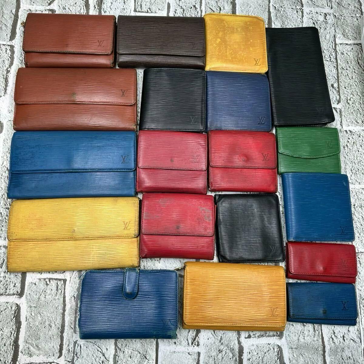 Top-down photo of many Louis Vuitton Epi wallets and small wallets in various colors arranged on a light brick-patterned surface.
