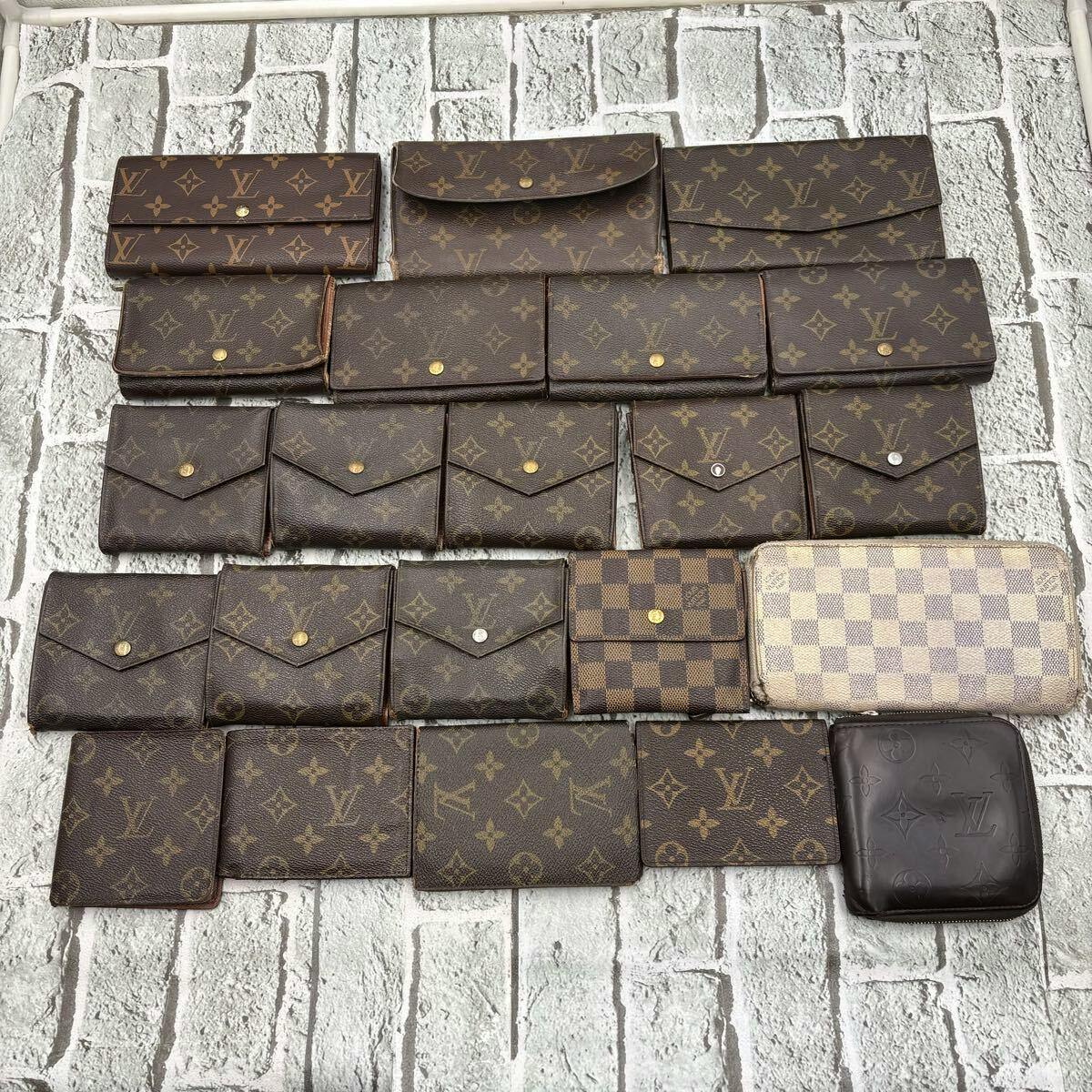Multiple Louis Vuitton monogram and Damier wallets from a 22-piece set laid out on a textured background.