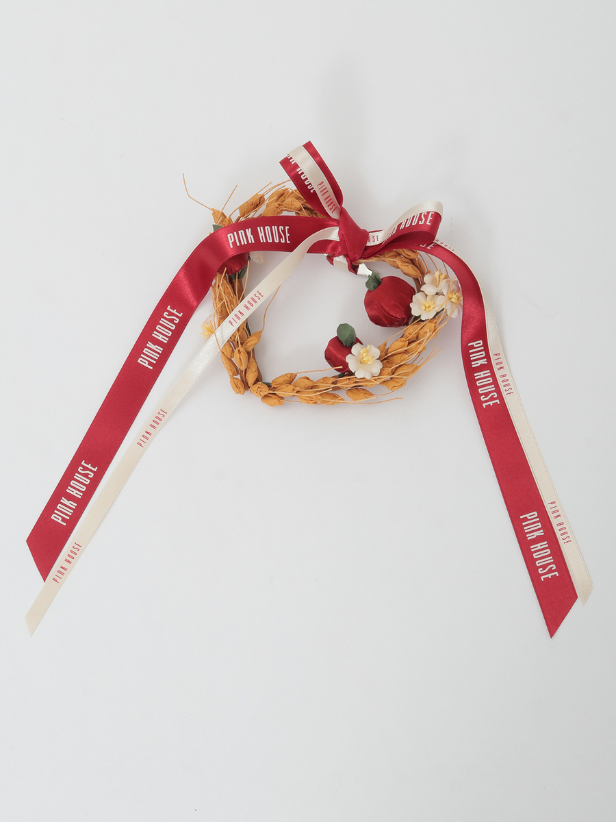 Polyester embroidered brooch with a braided wreath, red and cream ribbons, small red fabric buds, and white fabric flowers on a white background.