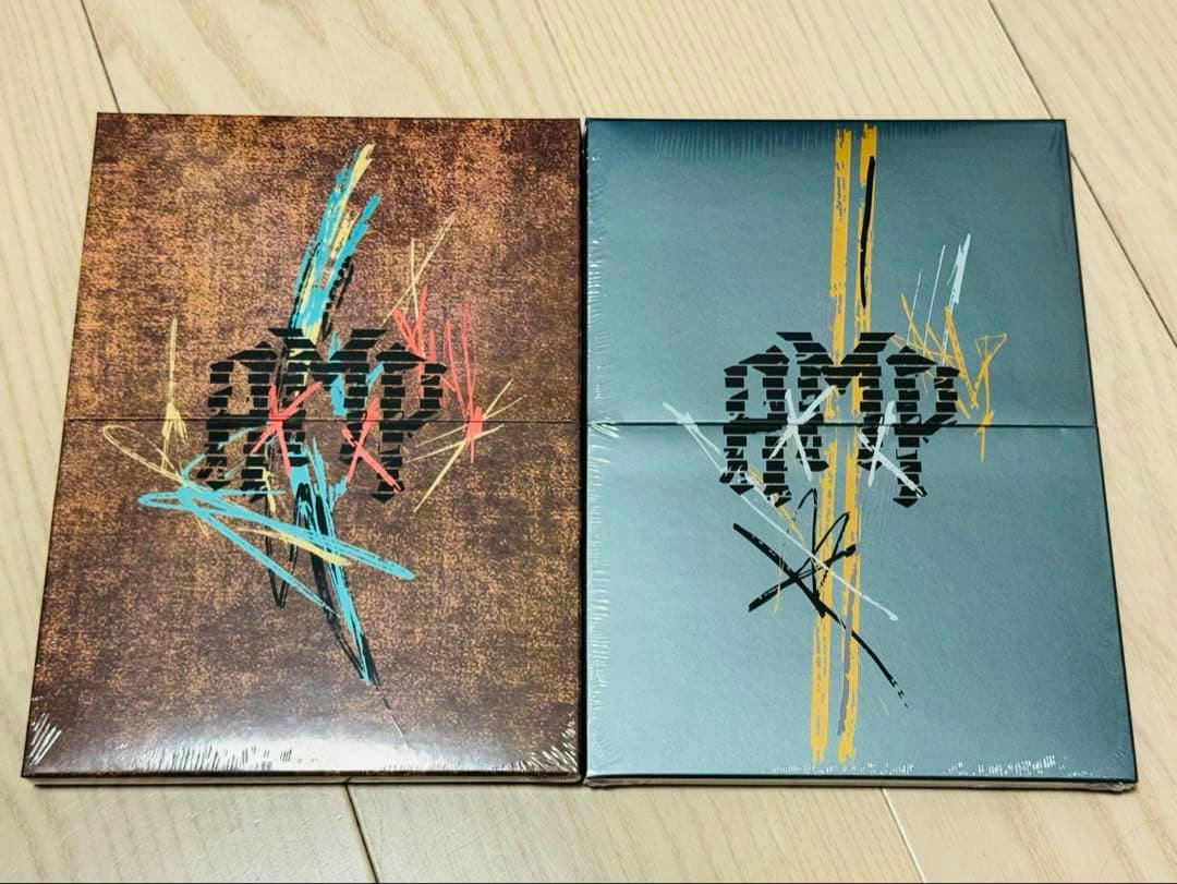 Two unopened AxMxP "Amplify My Way" CD albums in sealed boxes placed side by side on a wooden floor.