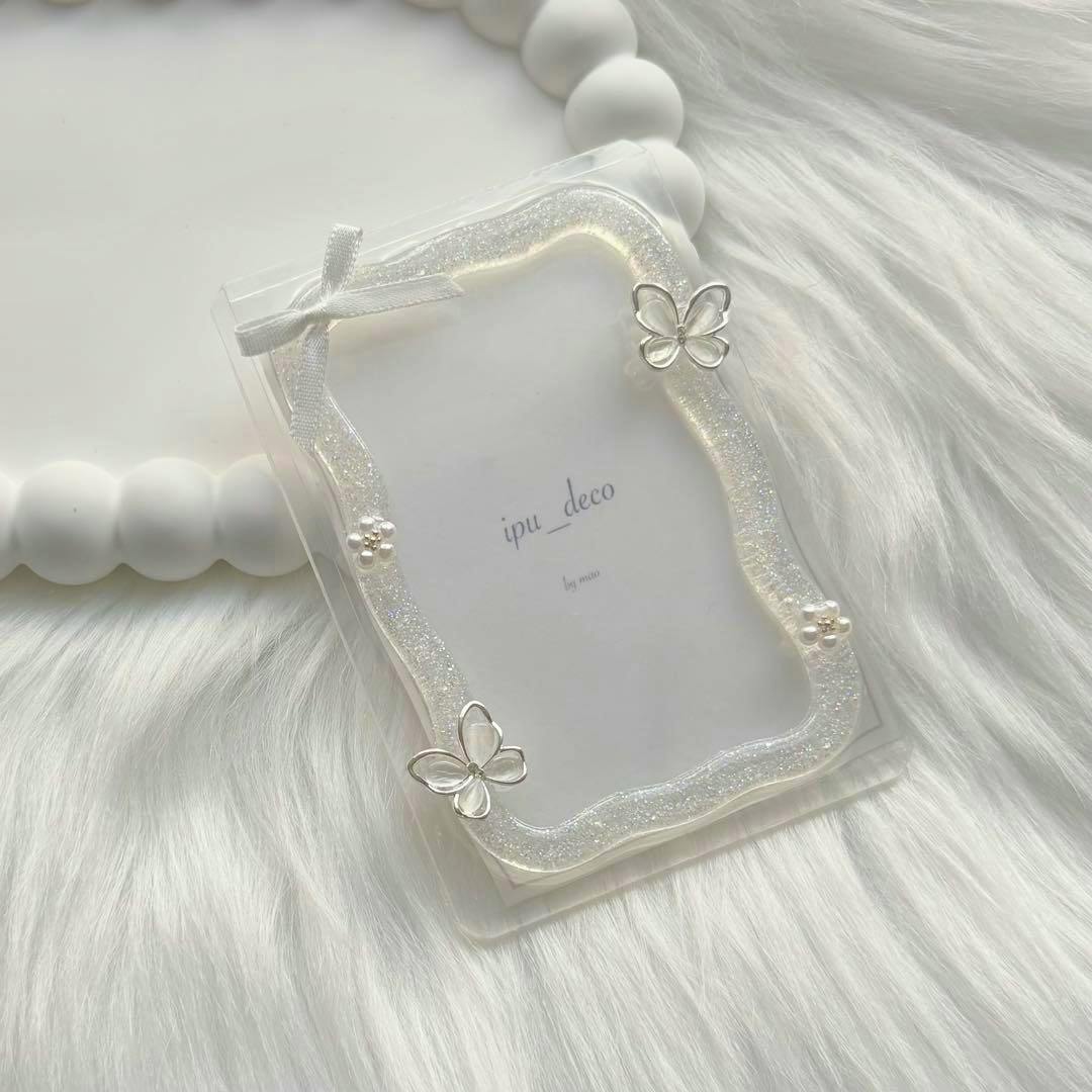 A clear B8 hard card case decorated with a glittery resin frame, small bow, butterfly charms, and pearl accents on a white fur background.