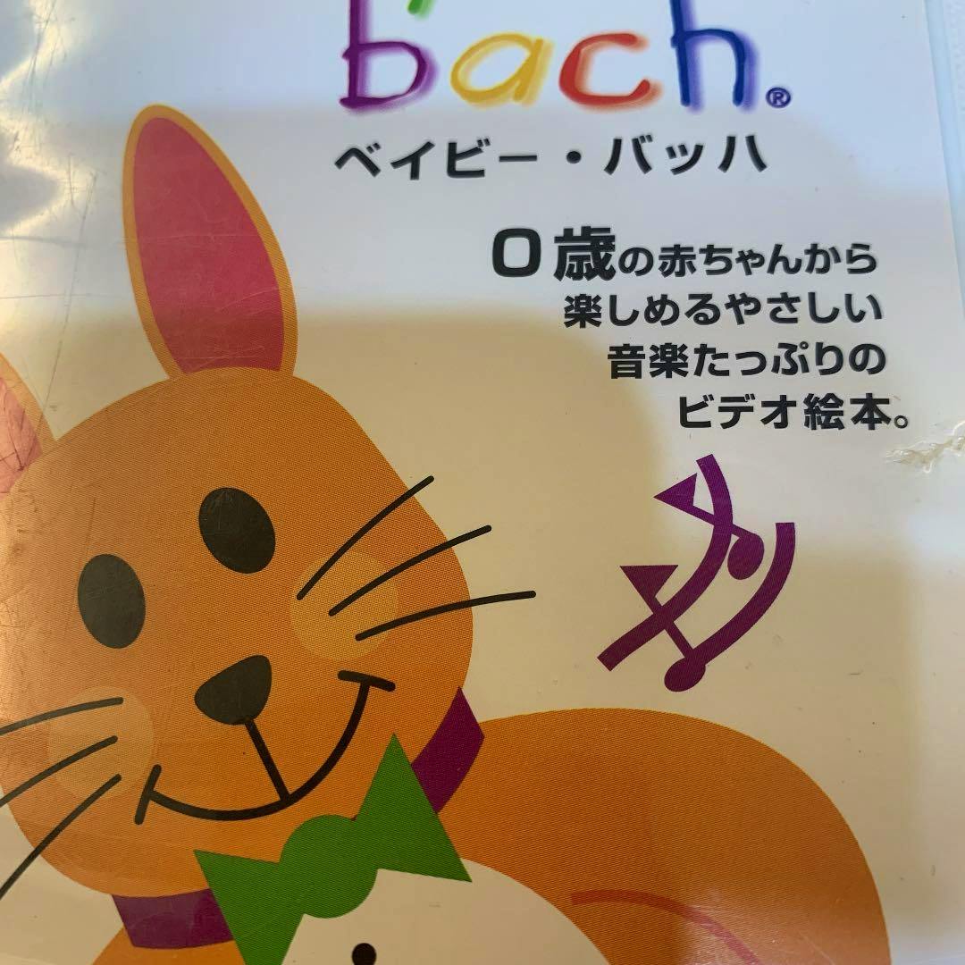 Close-up photo of the Baby Bach video picture book cover showing a smiling orange cat illustration and Japanese text stating it's for 0‑year‑old babies.