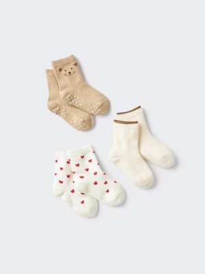 Three pairs of baby short socks displayed on a light background: a beige pair with a cat face, a cream pair with brown cuff trim, and a white pair with small red hearts.