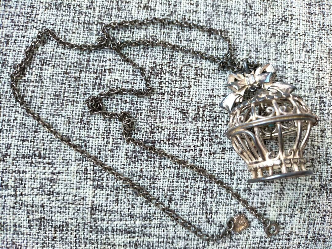 Birdcage pendant necklace with a chain laid on textured fabric background.