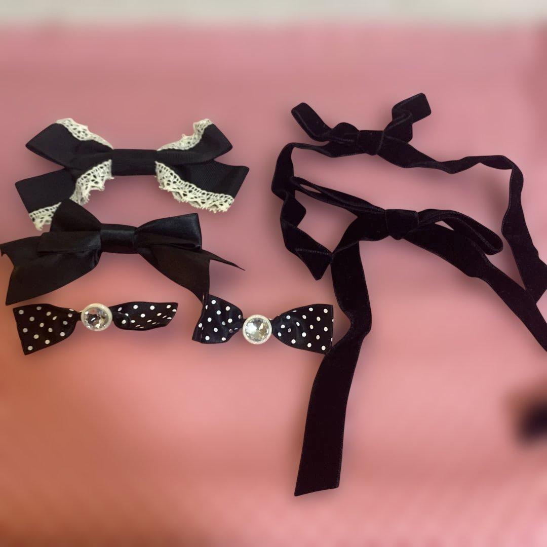 Photo of six black ribbon brooches, including lace-trimmed, velvet, and polka-dot styles, arranged on a pink surface.