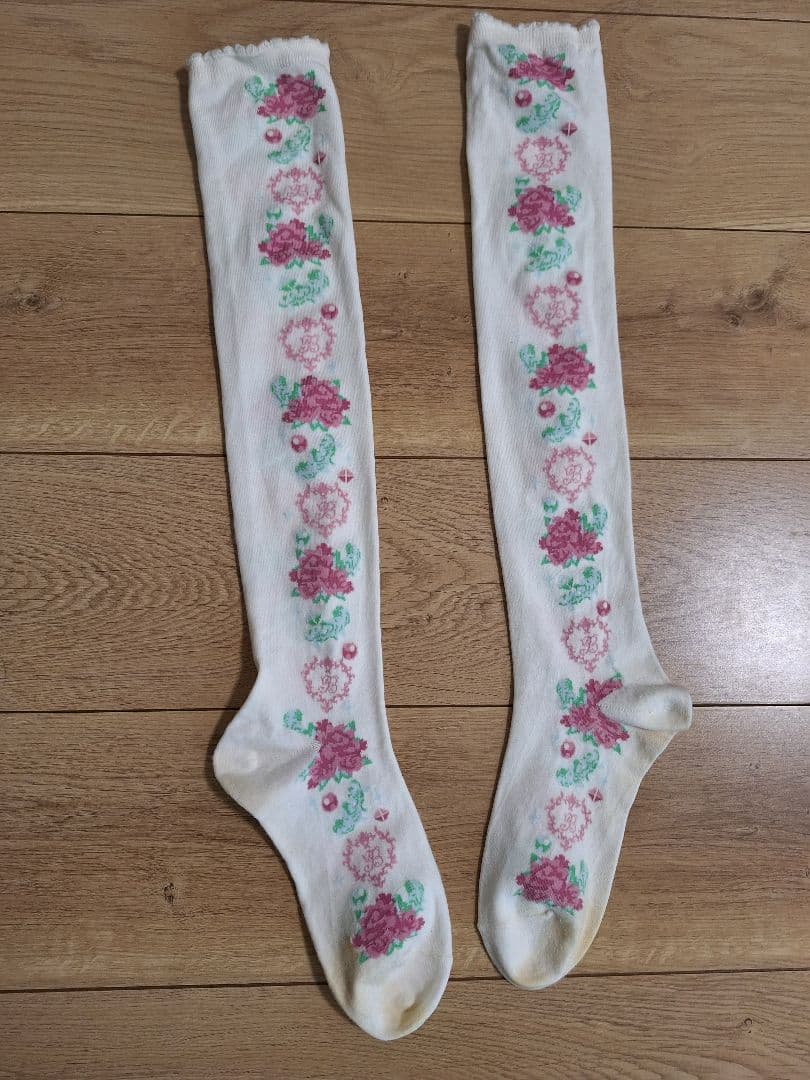 White women's cotton knee-high socks with a vertical pink rose pattern laid flat on a wooden floor.