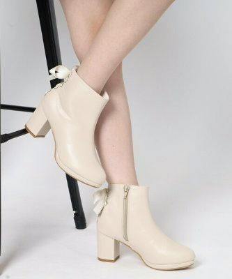 A model wearing cream synthetic leather ankle boots with block heels, a side zipper, and a back ribbon detail.