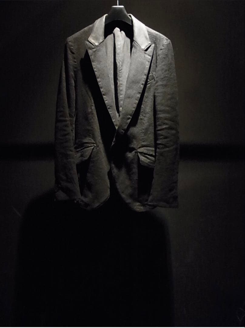 Front view of a men's linen jacket with leather-trimmed lapels hanging on a hanger against a dark background.