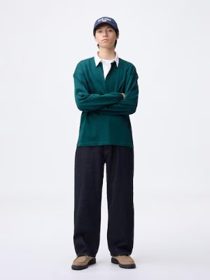 Front view of a model wearing the dark baggy jeans paired with a green long-sleeve top and a navy cap.