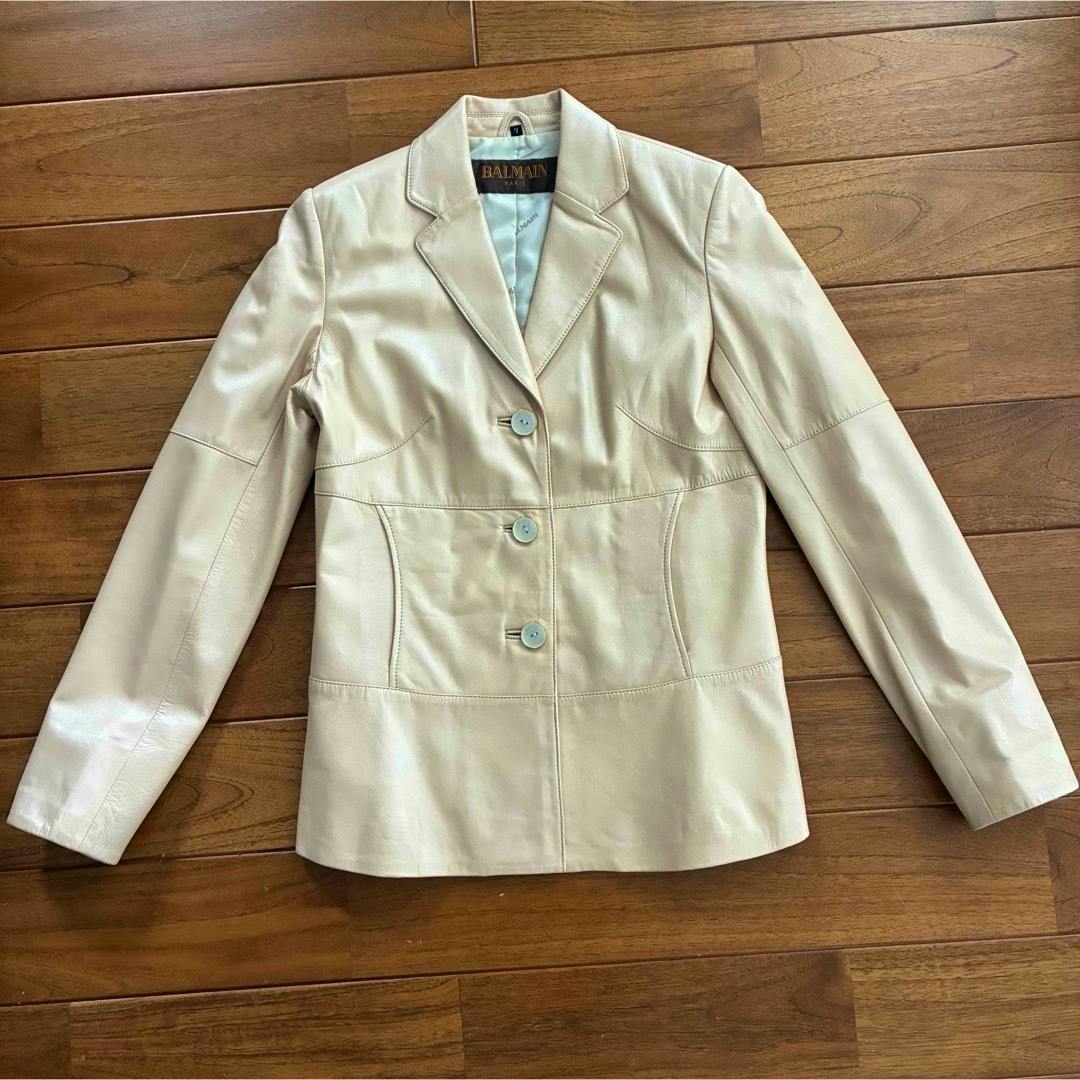 Front view of an ivory lambskin Balmain jacket laid flat on a wooden floor, showing three buttons and the Balmain label.
