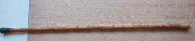 Full-length bamboo walking stick with a capped end laid on a light background.