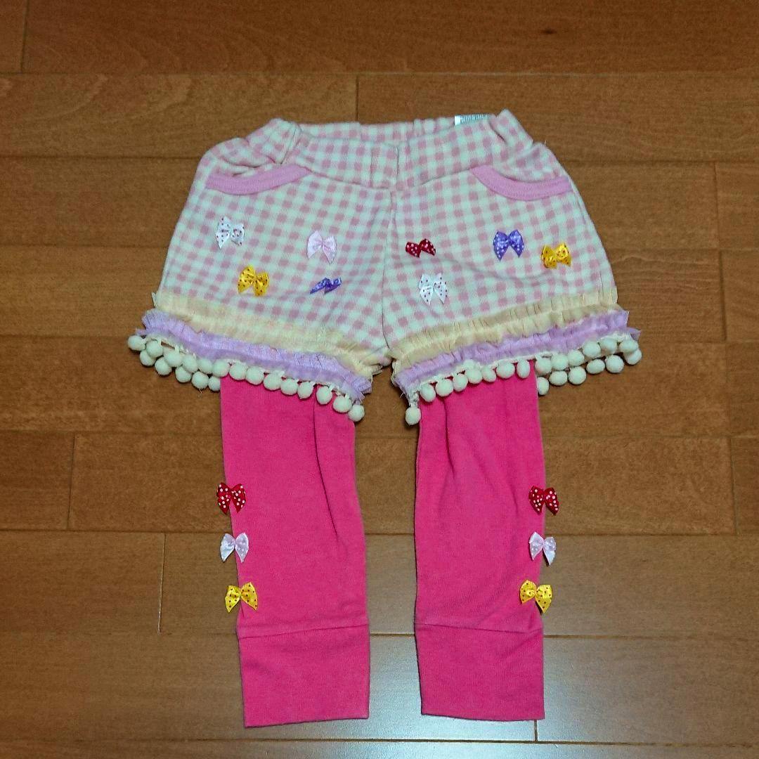 Pink children's cotton leggings with an attached checked skirt and small bow decorations laid flat on a wooden floor.