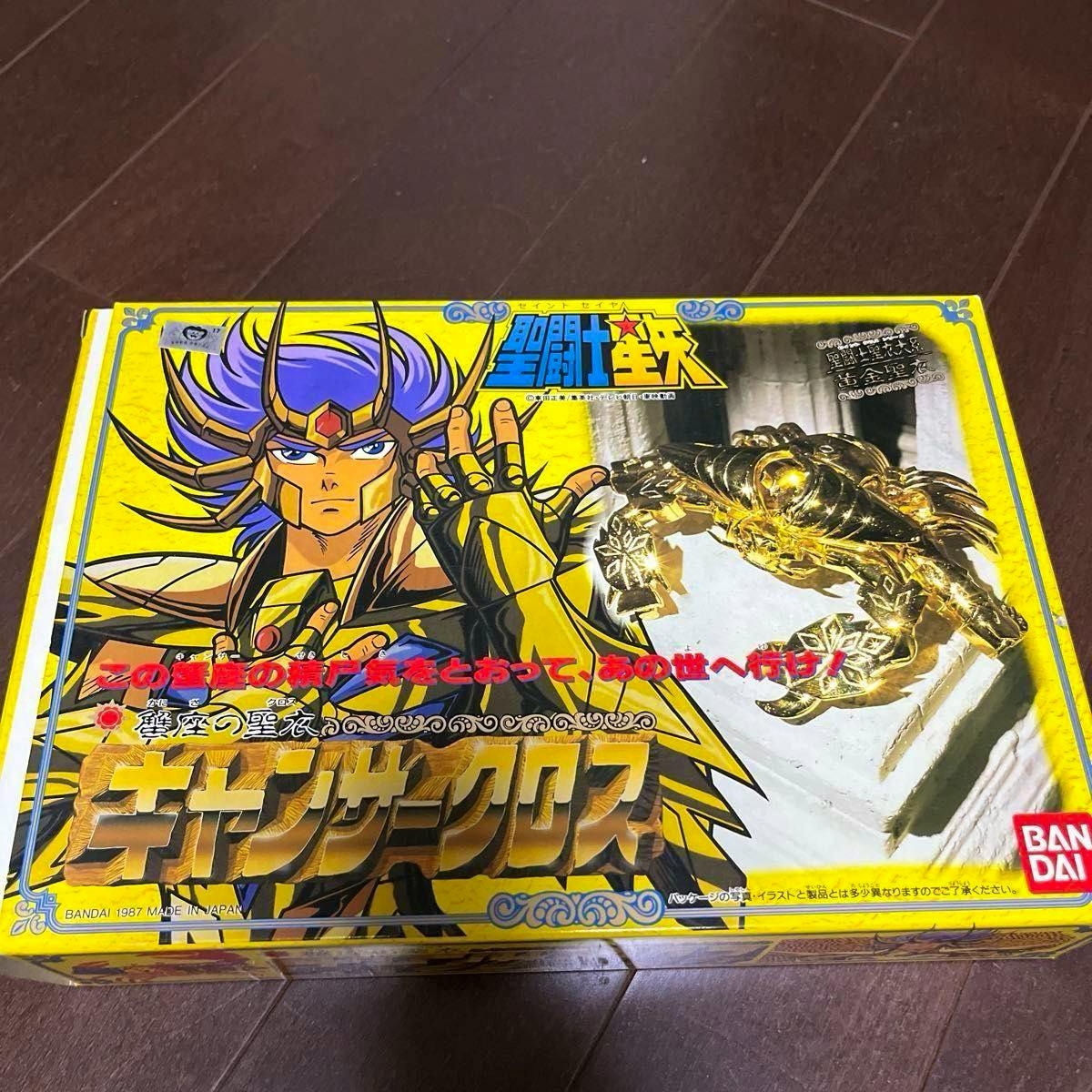Photograph of the product box showing character artwork and a photo of the gold Cancer Cloth armor.